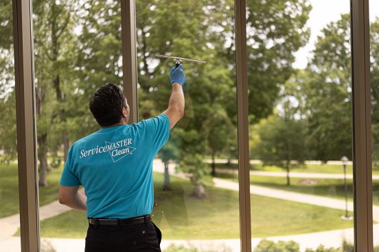 Technician in blue ServiceMaster Clean® uniform cleaning a window pane