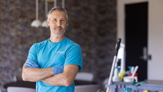 owner with arms crossed in front of cleaning supplies