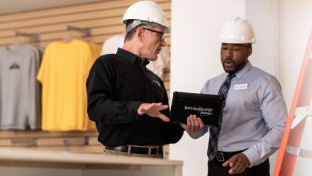 Two men with hard hats looking at a tablet