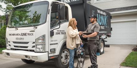 Smiling woman shaking hands with a junk hauler while a dog sits in between them