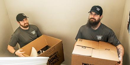 Two junk haulers carry boxes up the stairs during a job