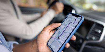 Passenger holds a phone in a car, showing a map app routing to a location 