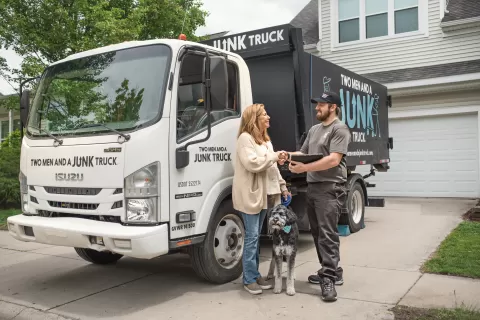 Smiling woman shaking hands with a junk hauler while a dog sits in between them