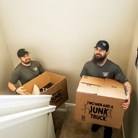 Two junk haulers carry boxes up the stairs during a job