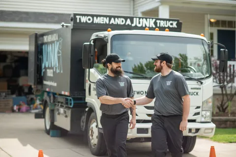 Two junk haulers shake hands in front of a TWO MEN AND A JUNK TRUCK