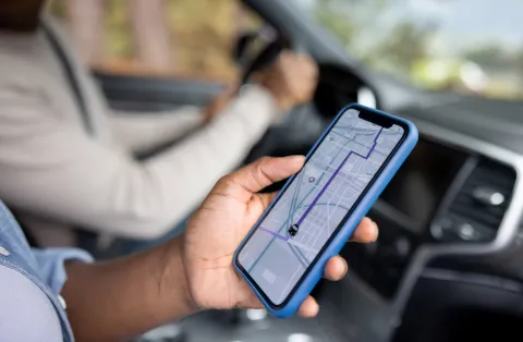 Passenger holds a phone in a car, showing a map app routing to a location 