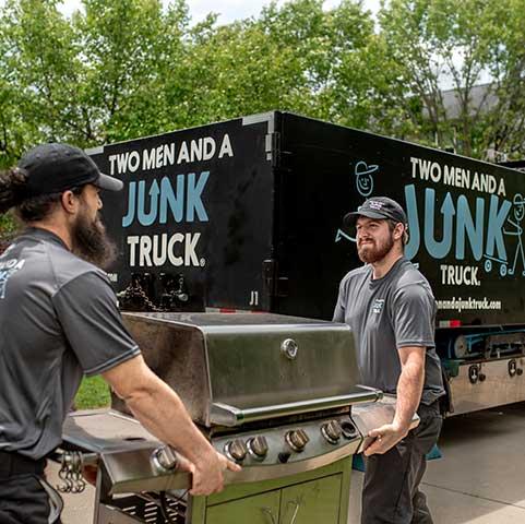 Junk removal team carrying grill by truck